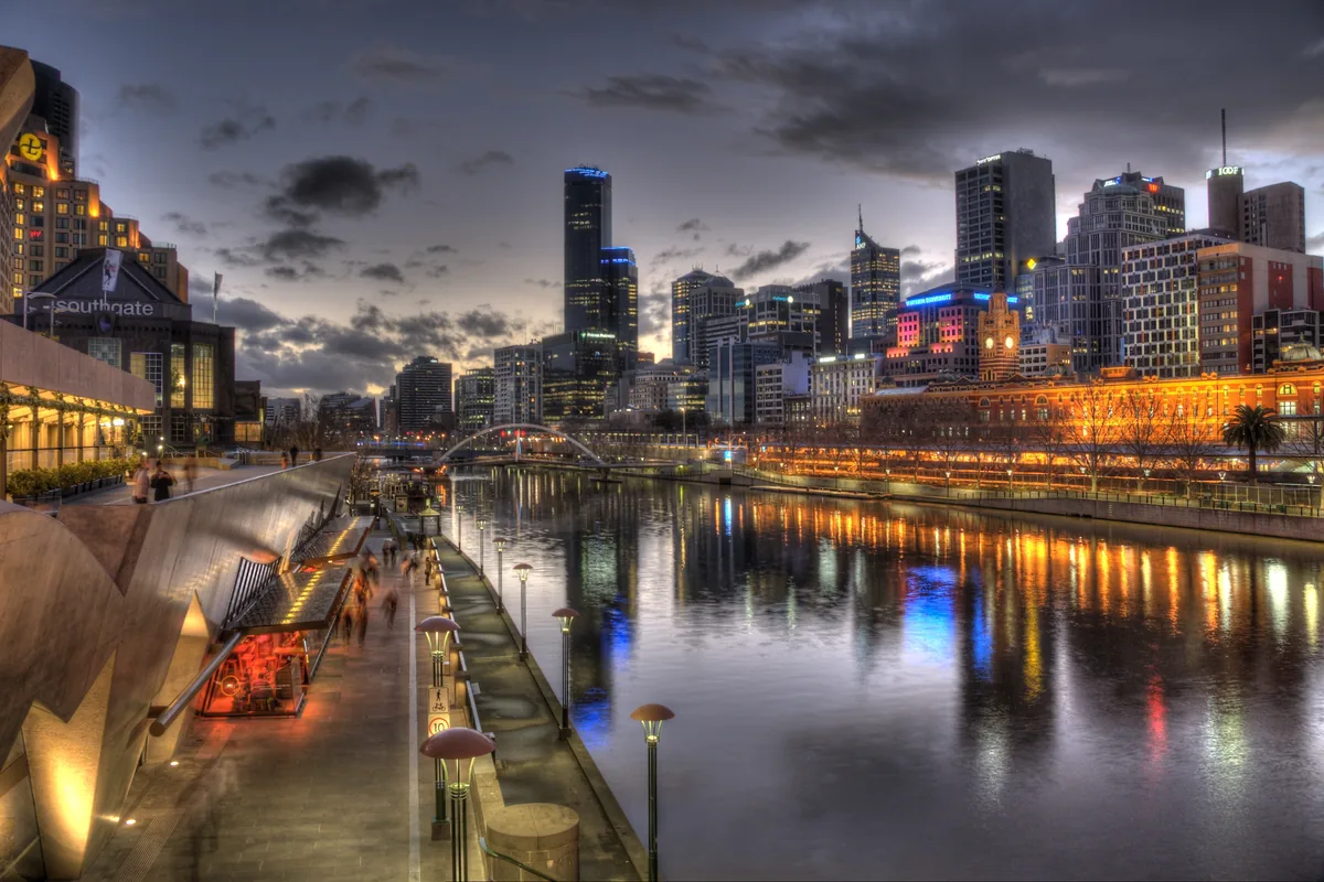 The Southbank promenade at dusk with a row of lit restaurants and the city skyline across the river.