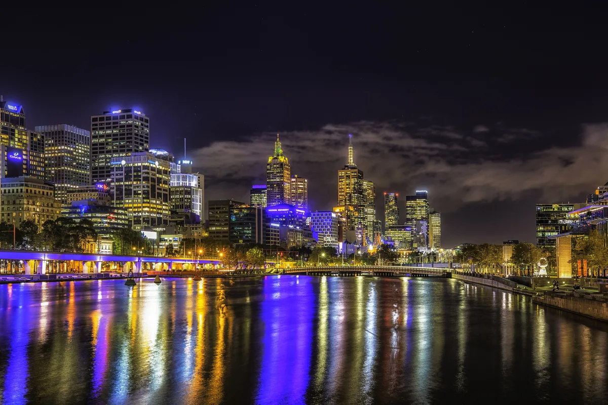 The Yarra at night with the lit city skyline and bright blue, gold and white reflections on the dark water.